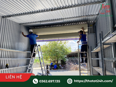 Thợ kỹ thuật đang kiểm tra và lắp đặt cơ chế mở tay cửa cuốn cho cửa khẩu độ rộng nhà xưởng.